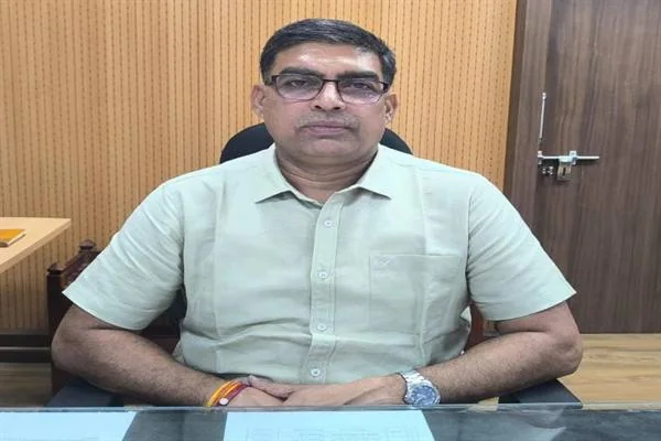 कार्यालय की कुर्सी पर बैठे हल्के हरे रंग की कमीज और चश्मा पहने एक अधिकारी