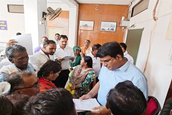 कलेक्ट्रेट के कमरे में लोगों से घिरे अधिकारी दस्तावेज और आवेदन देखते हुए